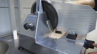 Mutfaktaki elektrikli yemek dilimleyicisinde sosis doğrayan aşçının kolunu kapat. Aşçının erkek eli mutfak restoranında jambon için kesme makinesi kullanıyor. Pizza pişirmek için gerekli malzemeleri hazırlama işlemi.