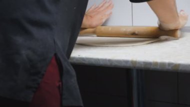 Close up arms of cook unrolling pastry with rolling pin on a kitchen table at restaurant. Male hands of chef rolling out pizza dough on a wooden surface at cuisine. Concept of cooking food. Slow
