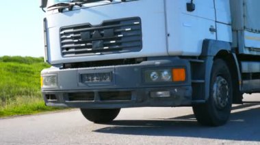 Kırsal yolda yüksek hızda giden beyaz kamyonun alt görüntüsü. Yaz günü kargo karavanıyla mal taşıyan bir kamyon. Yavaş çekim Düşük görünüm Kapat.