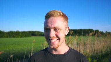 Kırsal kesimde ayakta duran ve kameraya bakan mutlu bir adamın portresi. Sakallı, genç ve yakışıklı bir adam. Yüzü elle kaplanmış gülüyor. Erkeklerin yüzlerindeki neşeli duyguları kapat. Yavaş çekim.