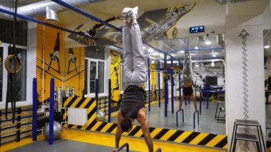 Güçlü kaslı adam modern spor salonundaki paralel barlarda amuda kalkıyor. Erkek jimnastikçi fitness merkezindeki düzensiz barlarda sert dublörlük yapar. Genç sporcu performansını sergiliyor. Sportif yaşam tarzı kavramı.