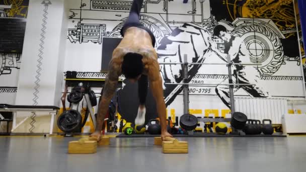 年轻的非洲裔美国运动员试图在室内木制地面设备的手倒立上做俯卧撑 肌肉发达的非洲小伙子在现代体育馆里苦练特技表演 健康和积极生活方式的概念 — 图库视频影像