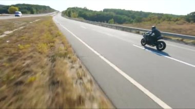 Anayolda motosiklet süren motosikletliyi takip edin. Motosikletli, kır yolunda motosikletiyle yarışıyor. Yolculuk sırasında bisiklet süren adam. Yolculukta özgürlük ve macera kavramı. Hava görüntüsü.