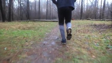 Erkek ayaklı sporcu, sonbahar ormanlarında yol boyunca koşuyor. Orman yolunda koşan genç sporcuların bacakları. Yağmurlu bir günde kardiyo antrenmanı yapan güçlü bir atlet. Etkin yaşam tarzı kavramı