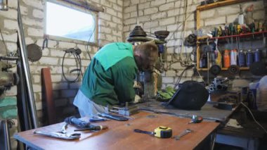 Koruyucu gözlüklü erkek tamirci atölyede üretim makinesi üzerinde çalışıyor. Garajda metal parçaları tamir eden üniformalı genç bir tamirci. Bakım hizmeti kavramı. Yavaşça kapat.