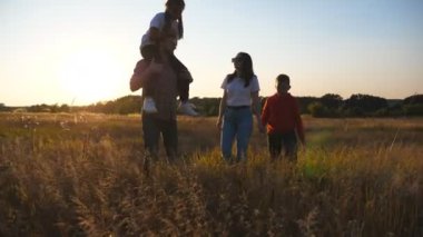 Gün batımında çim tarlasında yürüyen iki çocuklu genç bir çift. Küçük çocukları olan anne ve baba çayırların arasına gidiyor. Mutlu aile, güzel doğada birlikte vakit geçiriyor. Dolly vurdu.