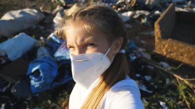 POV of small girl in protective mask going on landfill at countryside. Little disappointed child looks into camera walking on garbage at junkyard. Concept of environmental pollution problem. Slow mo.