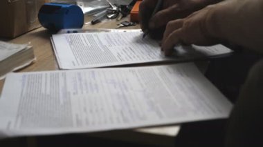 Kirli bir tamirci ya da tamirci elinde kalemle belgeye yeni bilgiler yazıyor. İşçinin erkek kolu masada yasal kağıtları imzalıyor. Sözleşmede imzası var. Not alıyorum. Yavaş çekim. Yakın çekim..