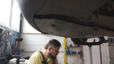 Profesyonel oto tamircisi atölyede özel elektrikli aletle cıvataları sıkılaştırıyor. Garajda kaldırma aracının altında çalışan bir adam. Sakallı tamirci araba tamir ediyor. Otomobil bakımı kavramı