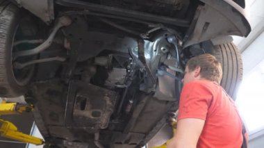 Tamirci, oto servisindeki bir kaldırma aracının altında çalışıyor. Profesyonel tamirci atölyede özel bir aletle araba tamir ediyor. Garajda otomobil tamir eden bir adam. Ulaşım bakımı kavramı.