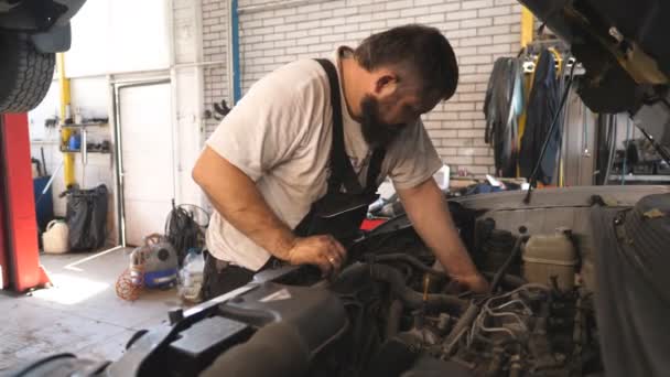专业汽车机械师在车篷下工作 维修工在车间或维修处修理车辆的发动机 有胡子的人在车库里检查汽车马达 维护和诊断的概念 — 图库视频影像