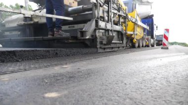 Yeni asfalt tabakasını yavaşça döşeyen bir paten. Kırsal alanda yol yapan özel makineler. Sıkıştırıcı otoyol yapımı. Ağır makineler yolu onarıyor. Yol çalışması süreci. Yol onarımı.