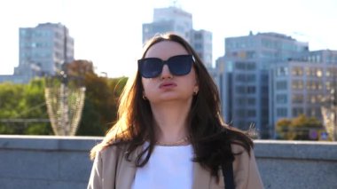 Yüzünde hoşnutsuzluk ifadesi olan güneş gözlüklü bir kadın portresi. Ciddi esmer kız şehir sokağındaki kameraya bakıyor. Mutsuz, sinirli iş kadını. Hüzünlü ya da rahatsız edici duygu kavramı.