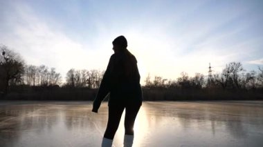 Artistik patenci kız gün batımında buz yüzeyinde paten kayıyor. Donmuş nehir veya gölde tek başına antrenman yapan genç bir kadın. Hanımefendinin becerileri gelişiyor ve kış aylarında boş vakitleri oluyor. Yavaş çekim.