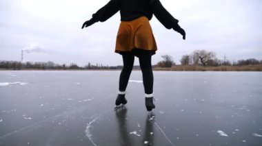 Bulutlu bir günde donmuş nehirde buz pateni yapan kadın patenci. Doğada buz pateni pistinde kayan artistik paten giymiş bir kadın. Soğuk kış havasında pratik yapan genç bir kız. Kış mevsiminde aktif boş zaman.