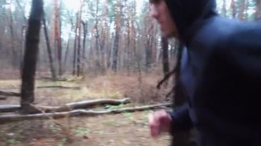 Sportif erkek koşucu sonbahar ormanında patika boyunca koşuyor. Orman yolunda koşan genç bir sporcu. Yağmurlu günlerde antrenman yapan güçlü bir sporcu. Sağlıklı aktif yaşam tarzı kavramı. Yavaş çekim.