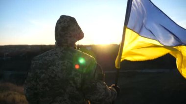 Ukrayna bayrağı sallayan tanınmamış Ukraynalı asker. Askeri üniformalı adam gün batımına karşı bayrak kaldırdı. Rus saldırısına karşı zafer. İstila direnci konsepti. Yavaş çekim.