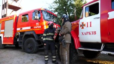 Genç profesyonel itfaiyeciler büyük kırmızı bir kamyonun yanında acil durum raporunu tartışıyorlar. İtfaiyeci şefi, astıyla itfaiye arabasının arka planındaki çalışmalar hakkında konuşuyor. Yavaş çekim.