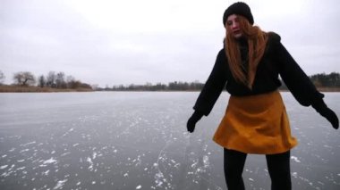 Donmuş nehirde kız eğitim rotasyonu yetenekleri. Dışarıda buz pateni pistinde kayan artistik patenlerle gezen genç bir kadın. Soğuk havada gölde sporcu kadın eğitimi. Dondurucu kış gününde aktif eğlence. Yavaş çekim