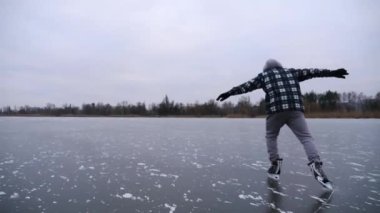Bulutlu bir günde donmuş nehirde kayan adam. Dışarıdaki buz yüzeyinde kayan artistik patenli genç adam. Soğuk kış havasında gölde sporcu eğitimi. Kış zamanı aktif bir eğlence. Yavaş çekim.