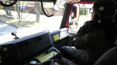 Professional fireman in uniform riding on a big truck to place of a fire. Young male firefighter in full equipment driving on fire engine to an emergency. Concept of saving lives and heroic profession