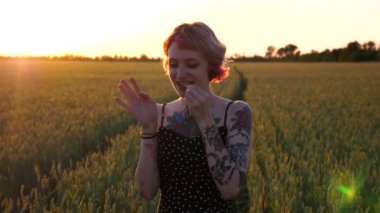 Tarlada yeşil buğday yiyen pembe saçlı komik hippi kadın portresi. Kulak tünelleri olan mutlu punk kızı arpa çayırında kameraya bakıyor. Özgürlük kavramı. Kapat..