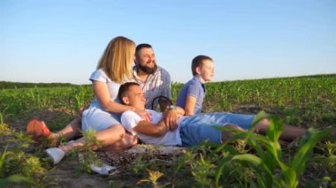 İki oğlu olan genç ebeveynler mısır tarlasında birlikte vakit geçiriyorlar. Çocuklu anne ve baba yeşil alanda oturuyor ve güzel doğanın tadını çıkarıyorlar. Aile mutluluğu kavramı. Yavaş çekim.