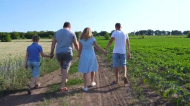 İki oğlu olan genç ebeveynler tarlaların yakınındaki kırsal yolda el ele yürüyorlar. Anne ve baba ve çocuklar yeşil çayırların yakınındaki yolda ilerliyorlar. Aile birlikte vakit geçiriyor.