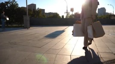 Genç bayan müşteriler alışverişlerden sonra kaldırımda yürürken alışveriş torbalarını tutarlar. Şık bir kadın şehir meydanında kağıt paketler taşıyor. Boş zaman ve boş zaman kavramı. Yavaş çekim.