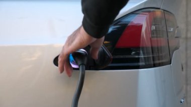 Erkek el elektrikli arabanın şarj aletini fişe takıyor. Adam şarj bataryalarından sonra elektrik kablosunu çıkarıyor. Modern teknoloji ve ekoloji dostu ulaşım kavramı. Kapat.
