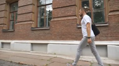 Başarılı bir iş adamı şehir caddesinde yürürken telefonla iş konuşur. Evrak çantalı genç adam ofise ya da toplantıya gidiyor. Kariyer konsepti. Yavaş çekim.