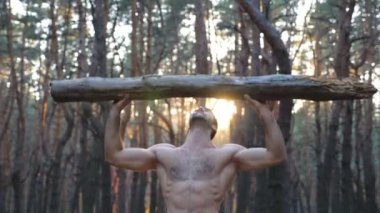 Kas yığını olan bir adam kafa çalıştırma ellerinin üzerinden ağır bir yük kaldırıyor. Gün batımında çıplak gövdeli güçlü bir adam dışarıda çalışıyor. Sporcu kütük kullanarak doğada egzersiz yapıyor. Spor ve aktif yaşam tarzı. Kapat..