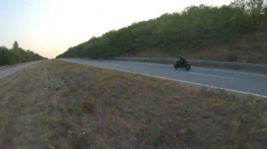 Anayolda motosiklet süren motosikletliyi takip edin. Motosikletli, kır yolunda motosikletiyle yarışıyor. Yolculuk sırasında bisiklet süren adam. Yolculukta özgürlük ve macera kavramı. Hava görüntüsü.