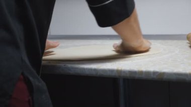 Aşçının erkek kollarını kapayarak mutfaktaki ahşap bir yüzeyde hamur işi oluşturuyorlar. Restorandaki mutfak masasında pizza için un hamuru şekillendiren şefin elleri. Yemek hazırlama kavramı. Yavaş çekim.