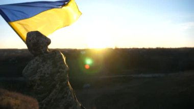Ukrayna ordusunun askeri tepede duruyor ve elinde Ukrayna bayrağı sallıyor. Askeri üniformalı tanınmayan adam gün batımına karşı bayrak kaldırdı. Rus saldırısına karşı zafer. İstila direnişi