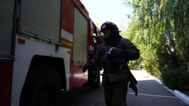 Genç itfaiyeciler üniformalarını hızla büyük kırmızı kamyondan çıkarıyorlar. Profesyonel itfaiyeciler yangını söndürmeye çalışıyor. Hayat kurtarma ve kahramanlık mesleği kavramı. Yavaşça kapat..