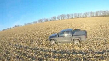Hasattan sonra tarladan geçen kamyonetin hava görüntüsü. Güneşli bir günde çayır boyunca giden off-road aracı. Gündüz vakti tarlaların arasında uçan bir araba. Manzara kırsal görünümü.