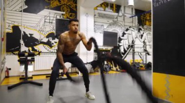 Dövüş halatlarıyla antrenman yapan güçlü Afrikalı sporcu fitness merkezinde. Modern spor salonunda sıkı çalışan kaslı Afro-Amerikan sporcusu. Sağlıklı ve aktif yaşam tarzı kavramı. Yavaş çekim.