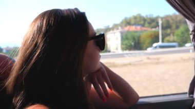 Güneşli bir günde otobüsle seyahat eden ve pencereye bakan güneş gözlüklü genç esmerin profili. Yolculuk sırasında çevreye hayran olan bir bayan yolcu. Tatil ya da gezi konsepti. Yavaşça kapat.