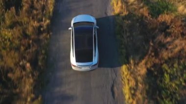 Yaz akşamları kır yolunda uçan elektrikli arabanın görüntüsü. Yeni bir SUV aracı otoban boyunca hızla ilerliyor. Çevre temiz otomobil otoyol boyunca elektrik yüküne biniyor. Üst görünüm.