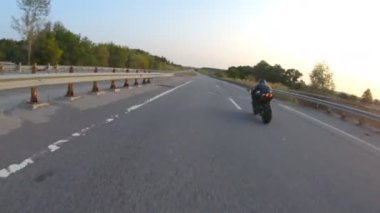 Günbatımında şehir yolunda motosikletle gezen motosikletliyi takip edin. Motosikletli otoyolda motosikletiyle yarışıyor. Yolculuk sırasında bisiklet süren adam. Yolculuk ve özgürlük kavramı. Hava görüntüsü.