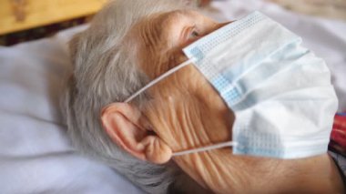 Virüsten koruyucu maske takan büyükannenin portresi. Hastanede yatarken üzgün bakışlı hasta bir kadın bir şeye bakıyor. Coronavirus 'tan sağlık ve güvenlik hayatı kavramı.