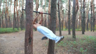 Atletik adam karın kaslarını çalıştırıyor yatay çıtada vücut kaldırıyor. Ormanda çalışan kaslı adam. Sporcu dışarıda egzersiz yapıyor. Spor anlayışı ve aktif yaşam tarzı. Yavaş çekim Dolly..