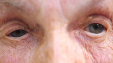Yaşlı bir kadın kameraya bakıyor ve gözlerini fena halde bozuyor. Şaşırtıcı duygular gösteren geniş gözlü, buruşuk kadın yüzünü kapatın. Yüzünde hayret ifadesi olan bir büyükanne. Yavaş çekim.