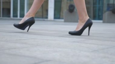 Yüksek topuklu ayakkabılı genç iş kadınının ayakları şehir sokağına çıkıyor. Yüksek topuklu siyah ayakkabılı zayıf kadın bacakları şehirde yürüyor. İşe giden bir kız. Düşük açı görünümü Yavaş çekim kapat.