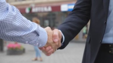 Bulanık şehir arka plan ile el sıkışan iki genç erkek arkadaşları. Kentsel ortamda birbirlerini tebrik emin iş adamları. Karşılıklı iş ortakları açık. Ağır çekim yakın çekim.