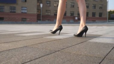 Güneşli bir günde şehir meydanında yürüyen yüksek topuklu siyah ayakkabılı zayıf kadın bacakları. Yüksek topuklu ayakkabılı genç iş kadınının ayakları şehir sokağına çıkıyor. Düşük açı görünümü Yavaş çekim kapat.