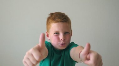 Mutlu kızıl saçlı çilli çocuğun portresi. Sevimli yakışıklı bebek başarıyı alkışlıyor ve baş parmağını kaldırıyor. Yüzünde neşe ifadesi olan erkek çocuğun duygularını kapat. Yavaş çekim.