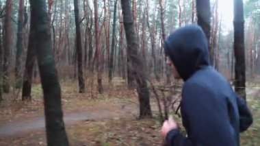 Sportif erkek koşucu sonbahar ormanında patika boyunca koşuyor. Orman yolunda koşan genç bir sporcu. Yağmurlu günlerde antrenman yapan güçlü bir sporcu. Sağlıklı aktif yaşam tarzı kavramı. Yavaş çekim.