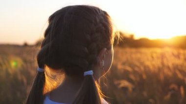 Güzel bir dişi çocuğun otlakta durup güzel bir akşam gün batımını izlediği arka manzara. Tasasız küçük kız yaz tarlasında dinleniyor. Bulanık arka plan. Özgürlük kavramı. Kapat..